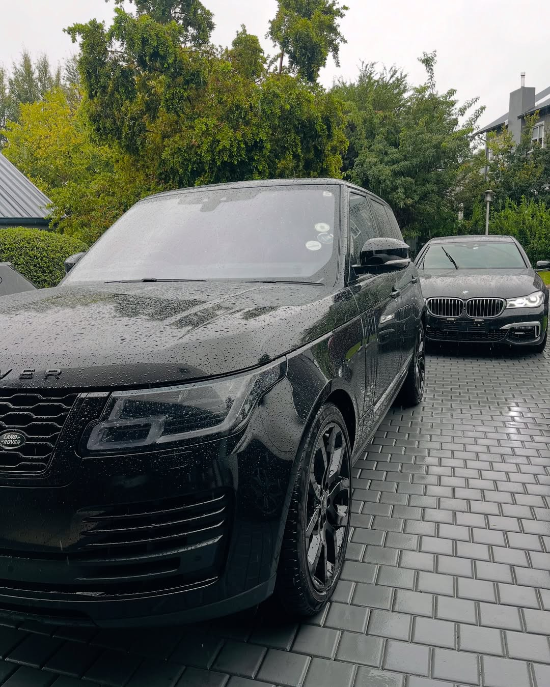 Black Range Rover and BMW sedan from the Mbewu Yolwazi fleet on a wet paved driveway